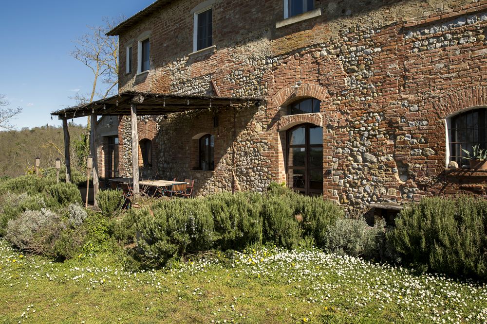 The stone facade of Siliano Alto in late afternoon light, olive trees along the wall